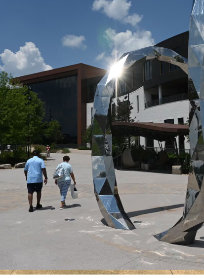 Two people walking across the MDS Strayer campus courtyard, past a mirrored sculpture